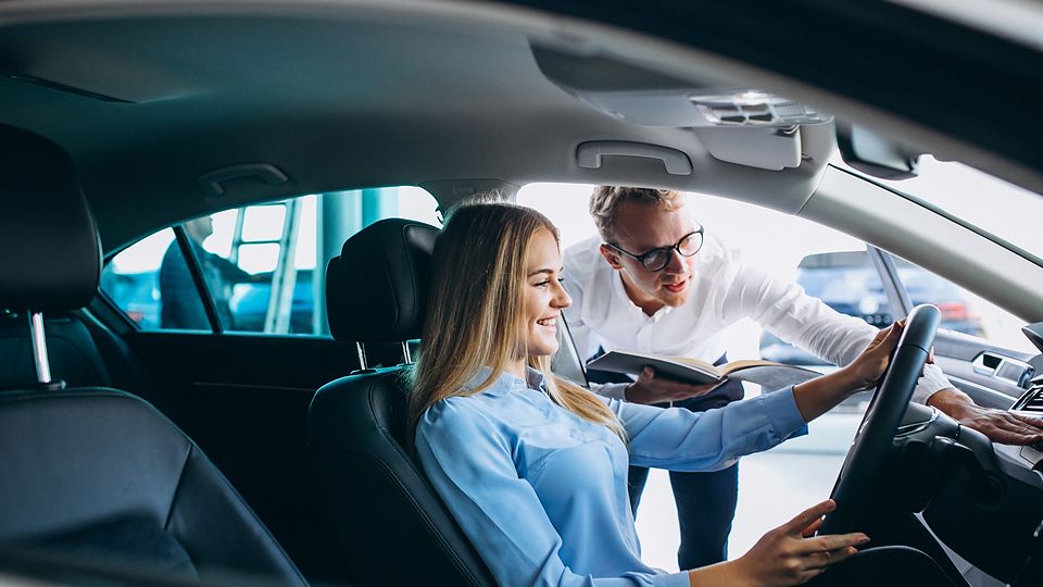 Consultora apresentando um carro na concessionária a uma cliente